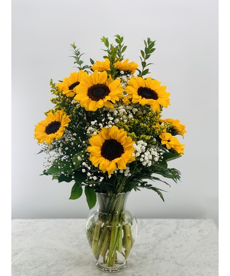 Seven sunflowers in a vase with greenery tied with yellow ribbon