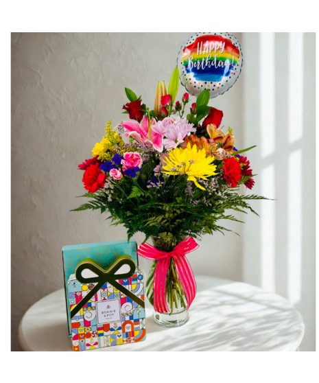 Bouquet of bright flowers in a glass vase beside a Happy Birthday! mylar balloon