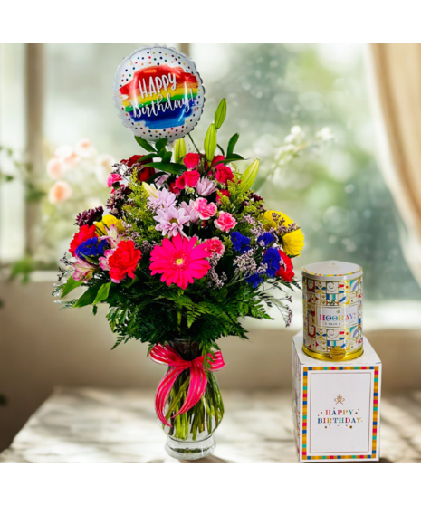 Bouquet of bright flowers in a glass vase beside a Happy Birthday! mylar balloon
