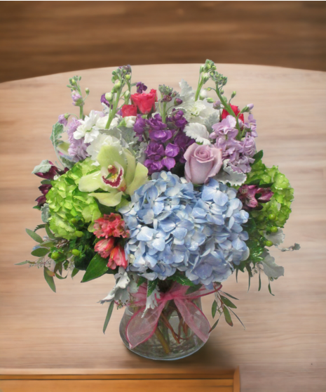 High-quality seasonal flowers in pastel shades tied with pink ribbon in a clear glass vase