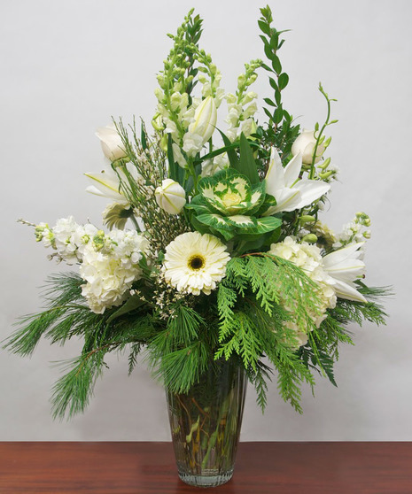 Pure white flowers and winter greenery in a clear glass vase.